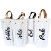 Canvas wine totes that either feature the word "bubbles," "white," "red" or "pink" on the outside of the bag. Each bag has a corresponding leather handle color. So, for example, the "pink" wine tote has a pink leather handle.