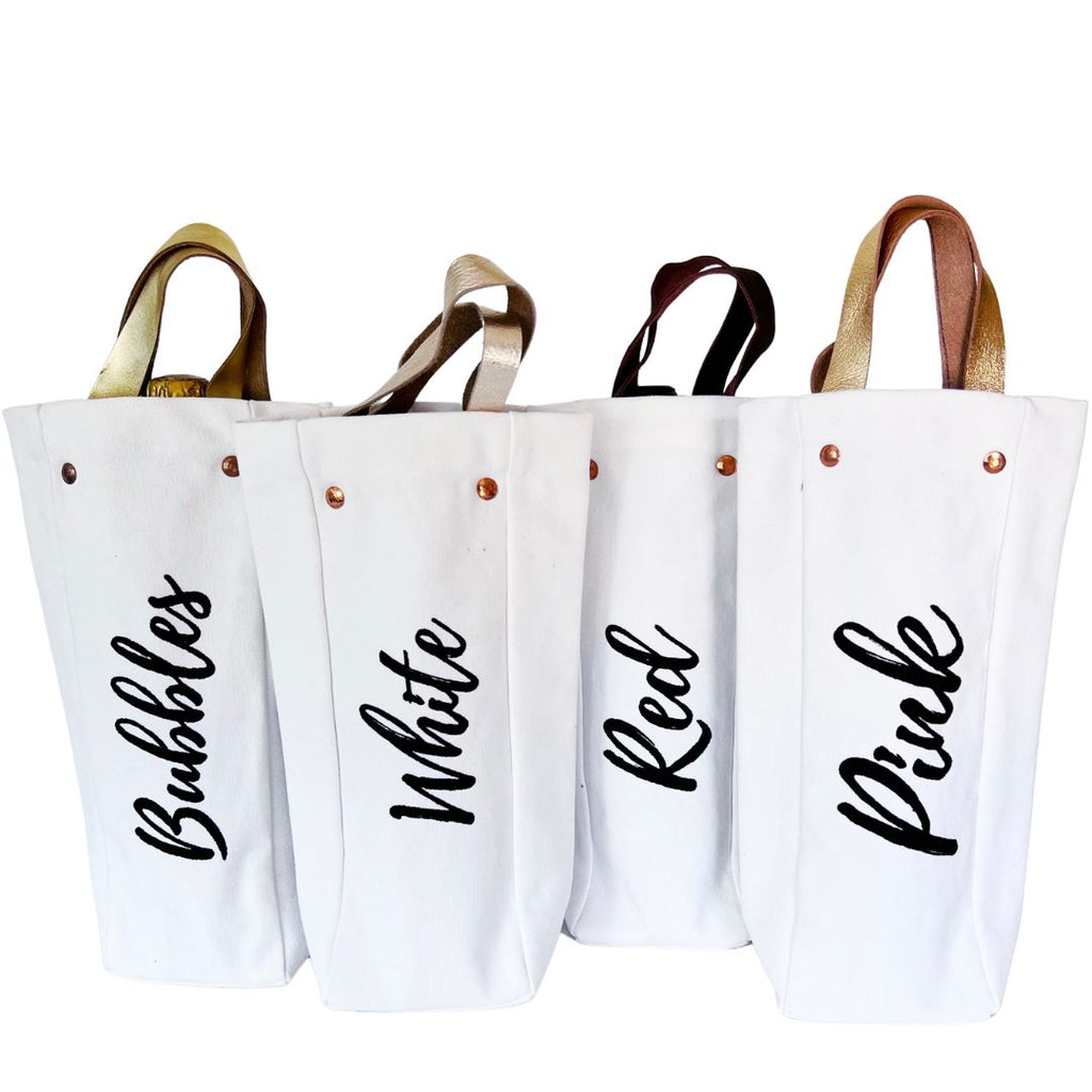 Canvas wine totes that either feature the word "bubbles," "white," "red" or "pink" on the outside of the bag. Each bag has a corresponding leather handle color. So, for example, the "pink" wine tote has a pink leather handle.